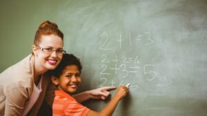 Teacher assisting boy to write on blackboard in classroom