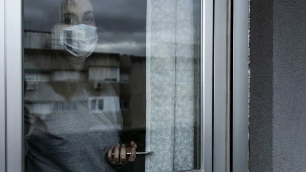 Grayscale picture of person behind glass door wearing mask