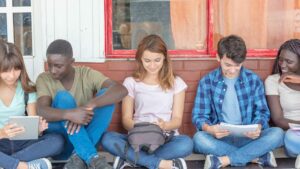 Multi ethnic group of teenagers using electronics and reading bo