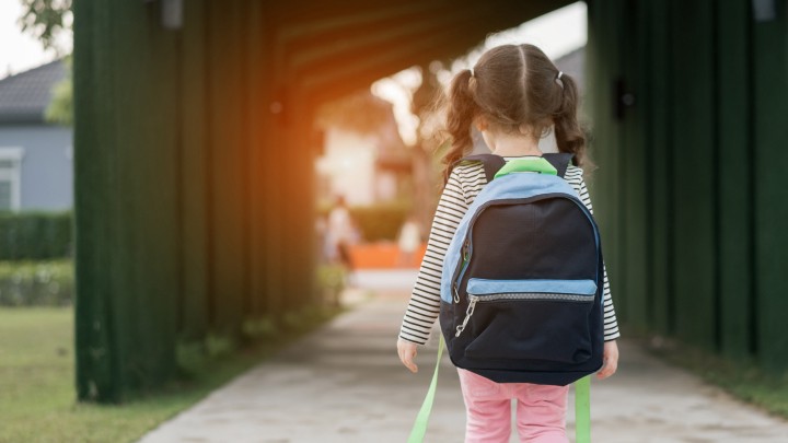 Kindergartener with backpack walking away from camera