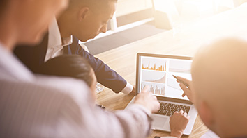 A group of professionals look at charts on a laptop computer.