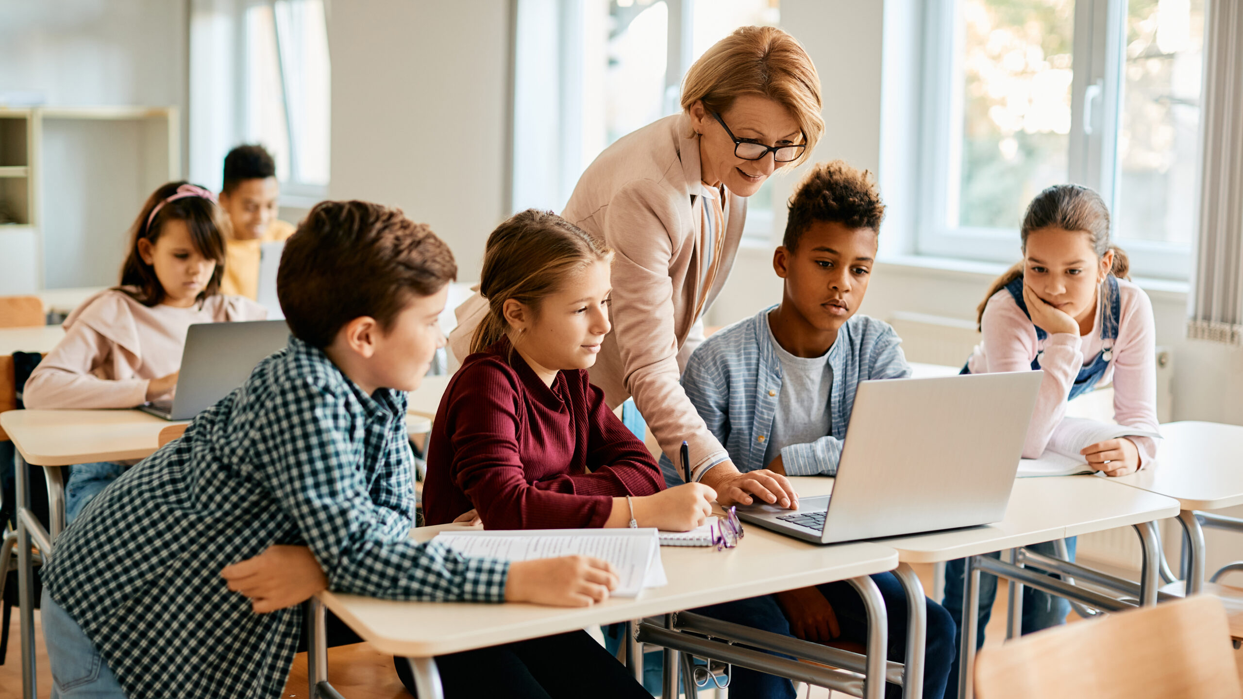 A teacher and students look at a laptop together in a classroom.