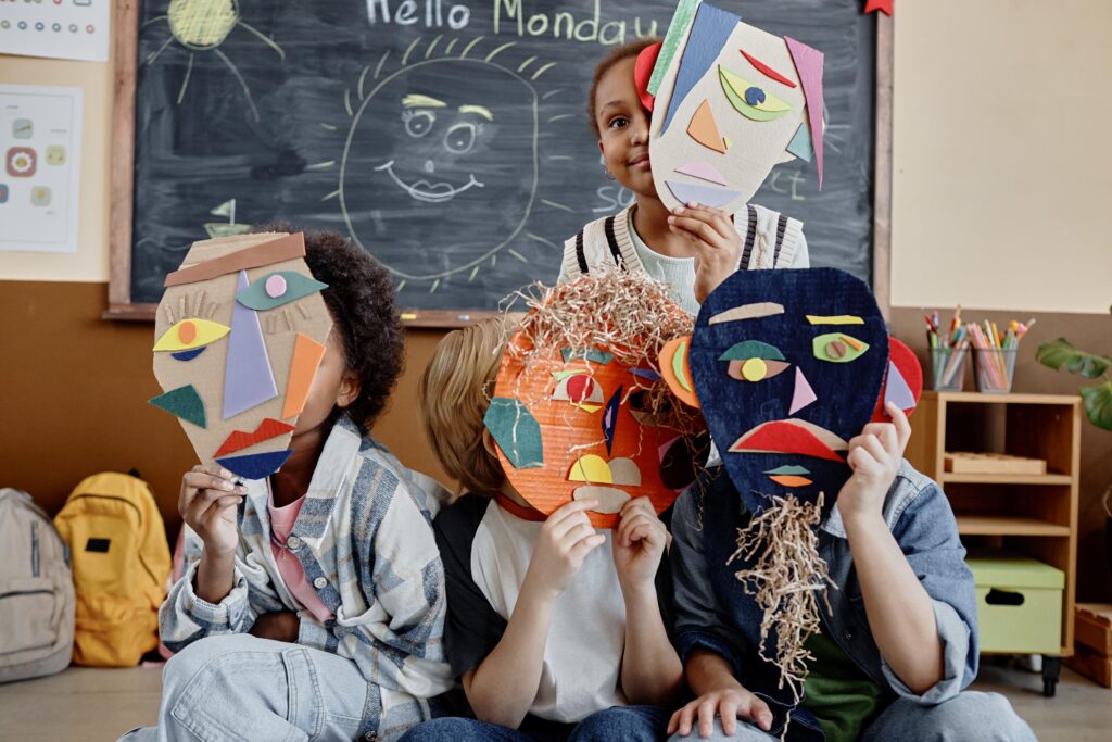 Young students wear colorful, handmade masks in a classroom.